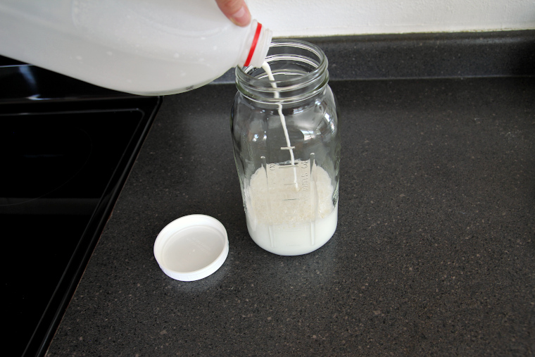pouring milk over grains to 6-cup mark on jar