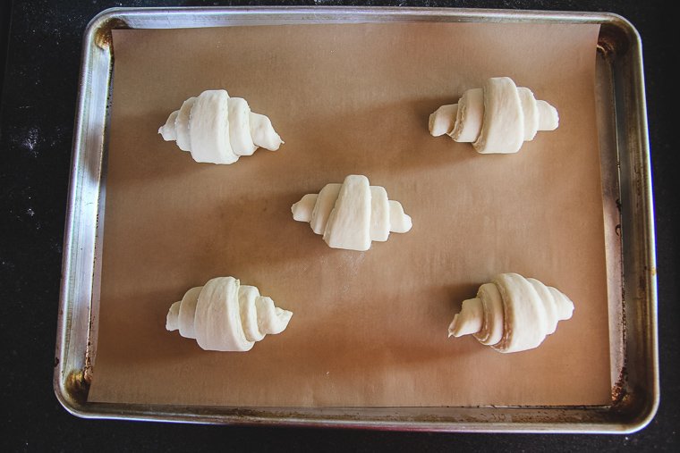 five croissants arranged on a parchment-lined half-sheet pan, ready to proof