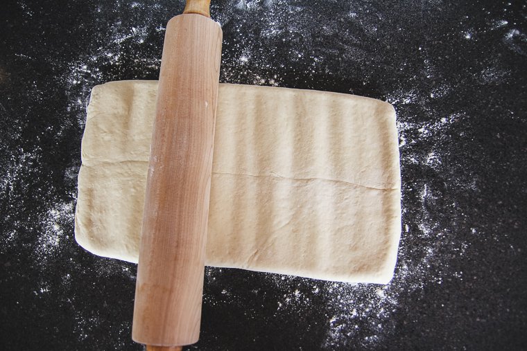 Pounding the dough with the rolling pin to begin to lengthen it while keeping the shape the same