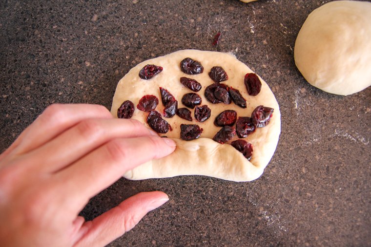 a hand rolling the dough over the dried blueberries to pre-shape the bagel