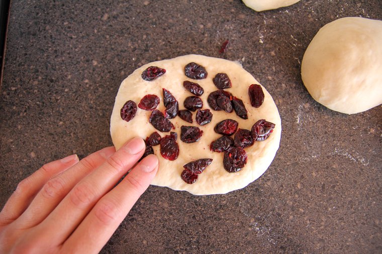 a hand pressing dried blueberries into the bagel dough