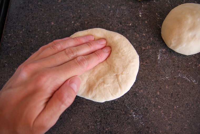 fingers pressing a dough ball into a flat circle