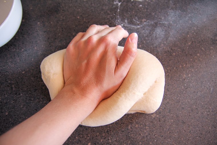 a hand kneading the stiff bagel dough