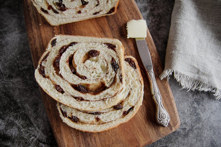 two slices of sourdough cinnamon raisin bread with a table knife and a pat of butter