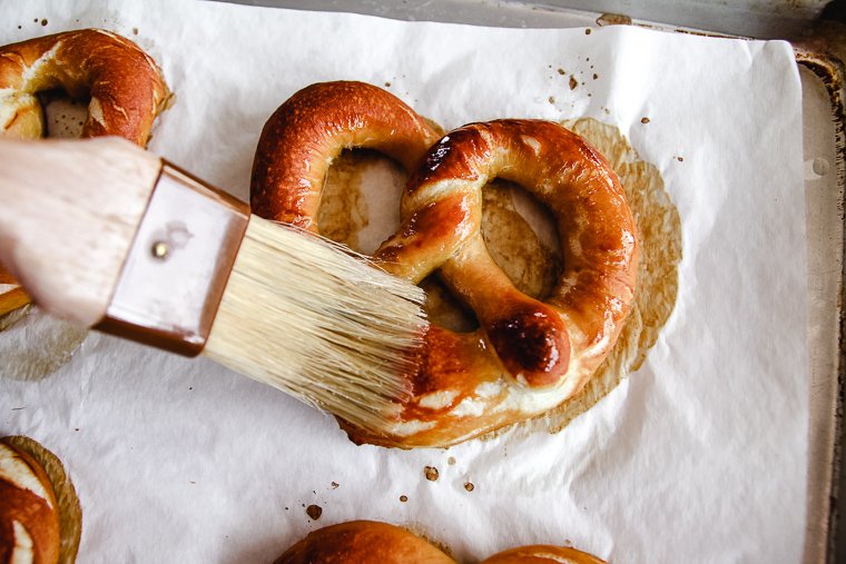 brushing a baked pretzel with melted butter