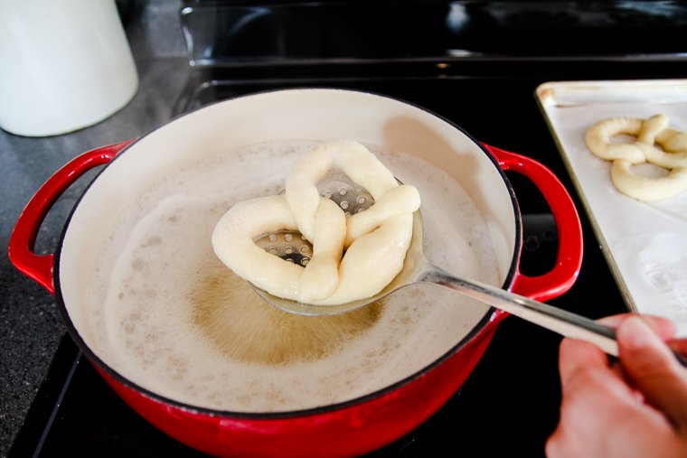 pulling a pretzel out of the boiling pot with a spider strainer spoon