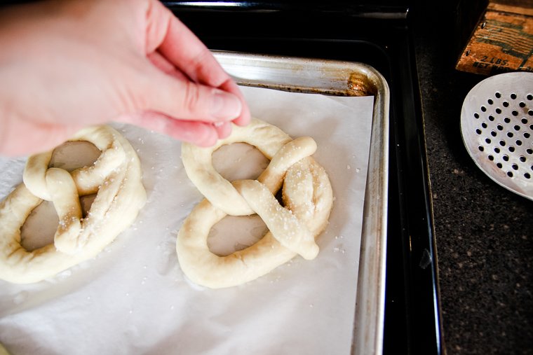 sprinkling a boiled pretzel with kosher salt