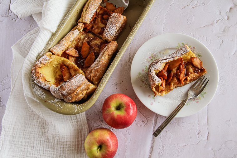 A sliced German apple pancake sitting next to two red apples