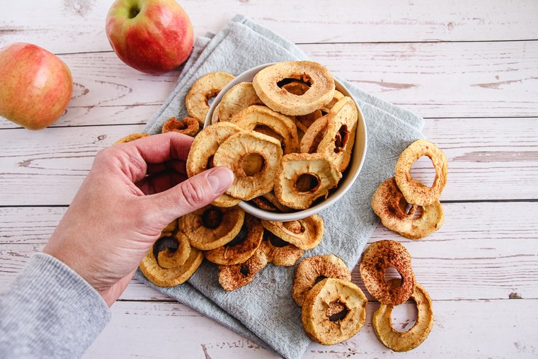 a hand grabbing some dried apple rings out of a bowl