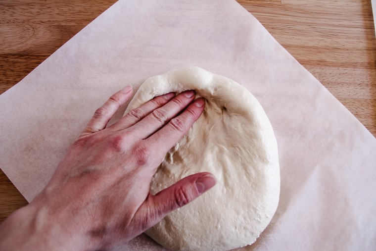 beginning to press out pizza dough ball into the correct shape