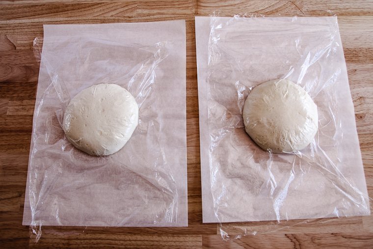 pizza dough balls after proofing on parchment paper while covered with plastic wrap