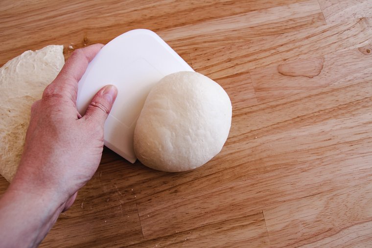 pushing the pizza dough against the counter with a dough scraper to tighten the shape