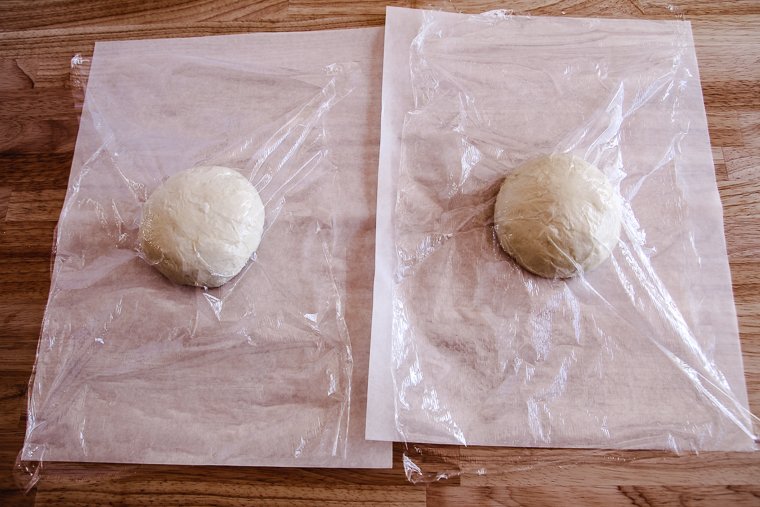 pizza dough on parchment paper with plastic wrap ready to proof