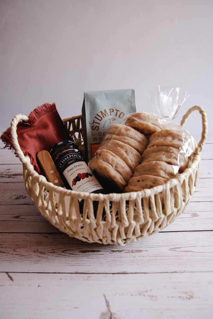 homemade bread gift basket made with english muffins, fruit spread, coffee beans, a wooden spreader, and a cloth napkin