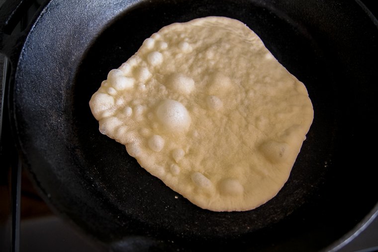 cooking sourdough naan in a cast iron skillet (the surface has bubbled)