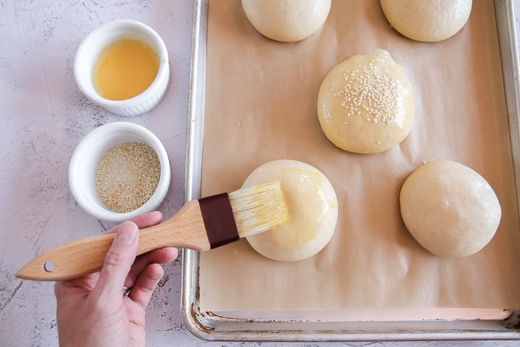 brushing sourdough buns with egg wash and sprinkling with sesame seeds