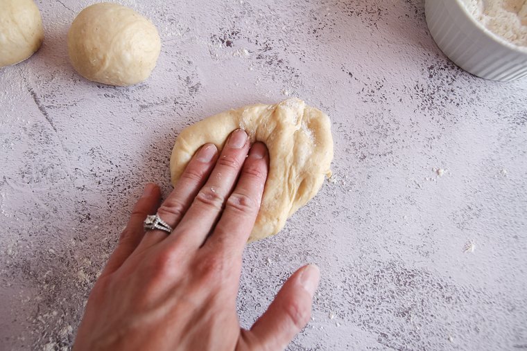 degassing a piece of dough before shaping it into a hamburger bun