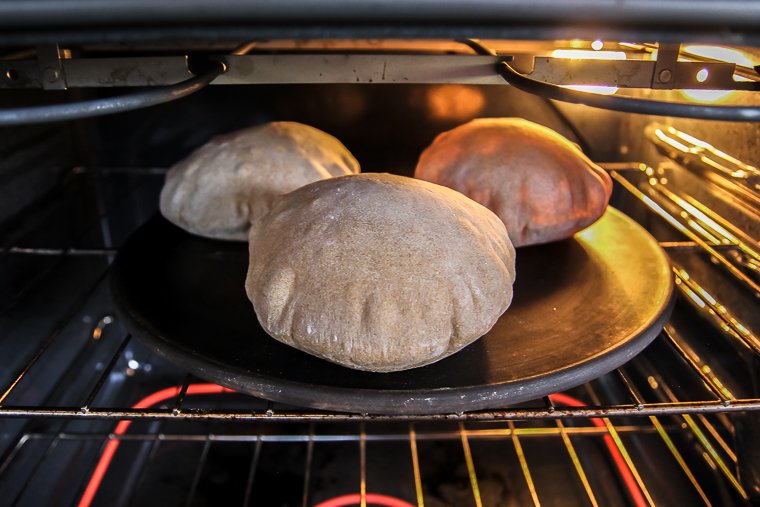 three whole wheat pitas puffed up in the oven on a baking stone