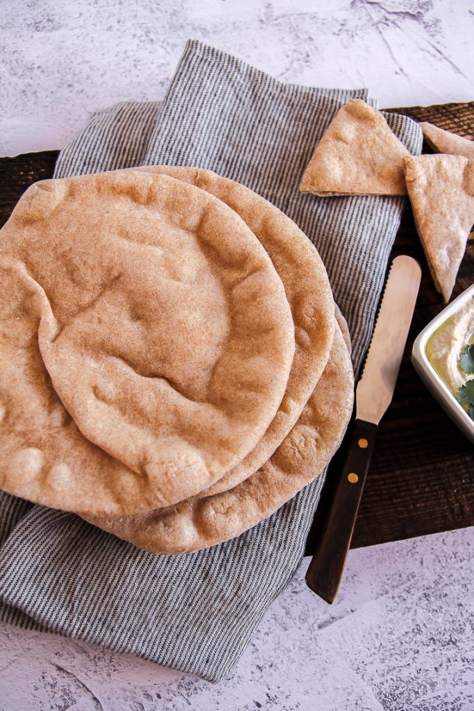 a stack of homemade sourdough pita bread on a board with a dish of hummus