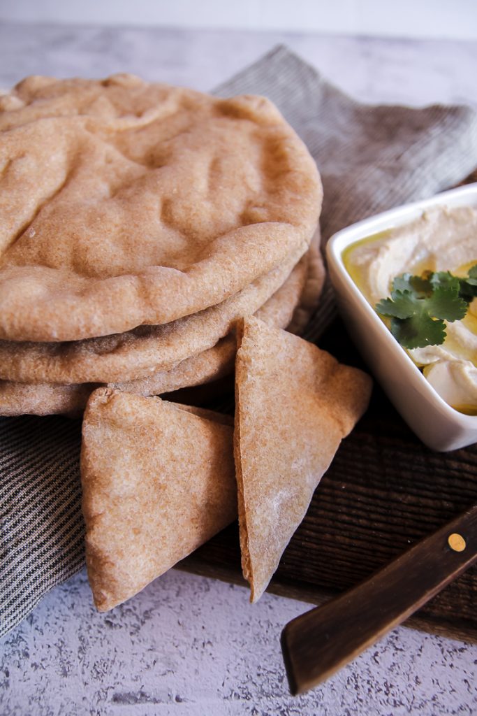 a stack of pita bread next to a dish of hummus and two triangle-shaped pieces of pita