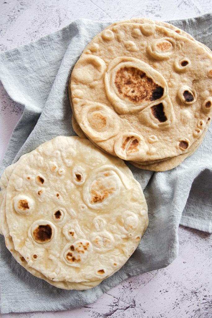 one stack of whole wheat sourdough discard tortillas and one stack of white flour tortillas on a light blue tea towel