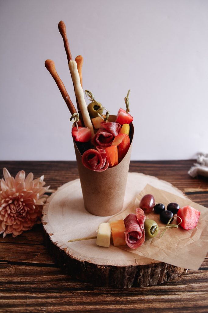 a charcuterie appetizer in a cup on a raw wood slice serving board