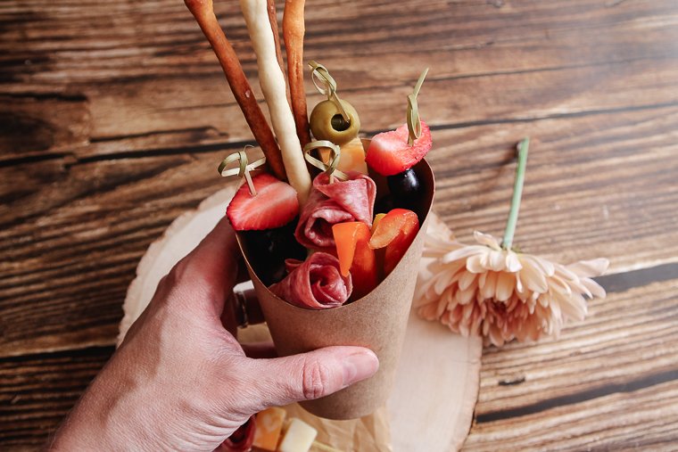 a hand grabbing the charcuterie cup