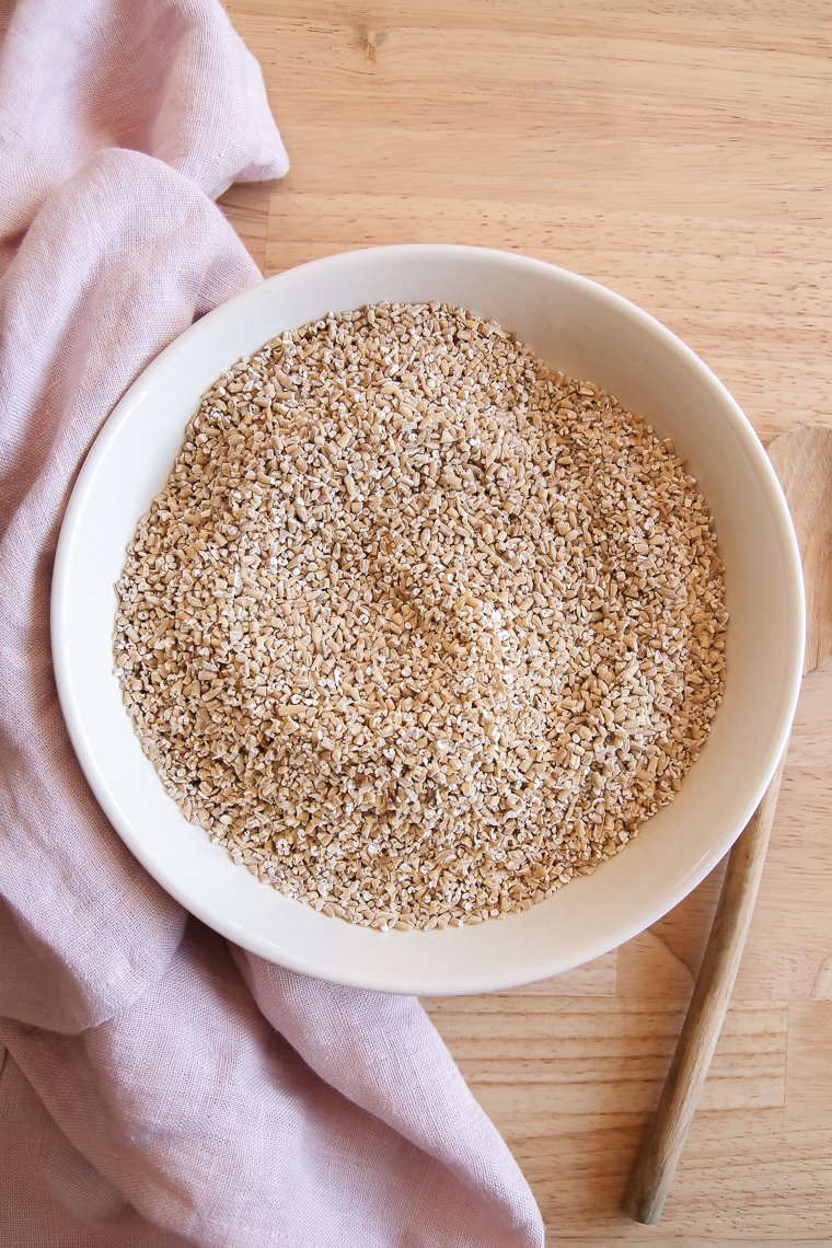 raw steel cut oats in a cream-colored bowl next to a pink cloth napkin