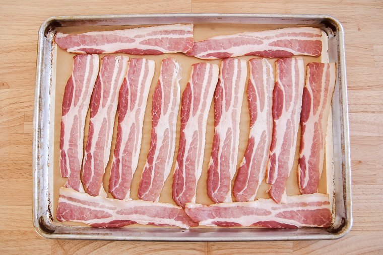a sheet pan with parchment paper and a single layer of bacon slices, ready to be baked the oven