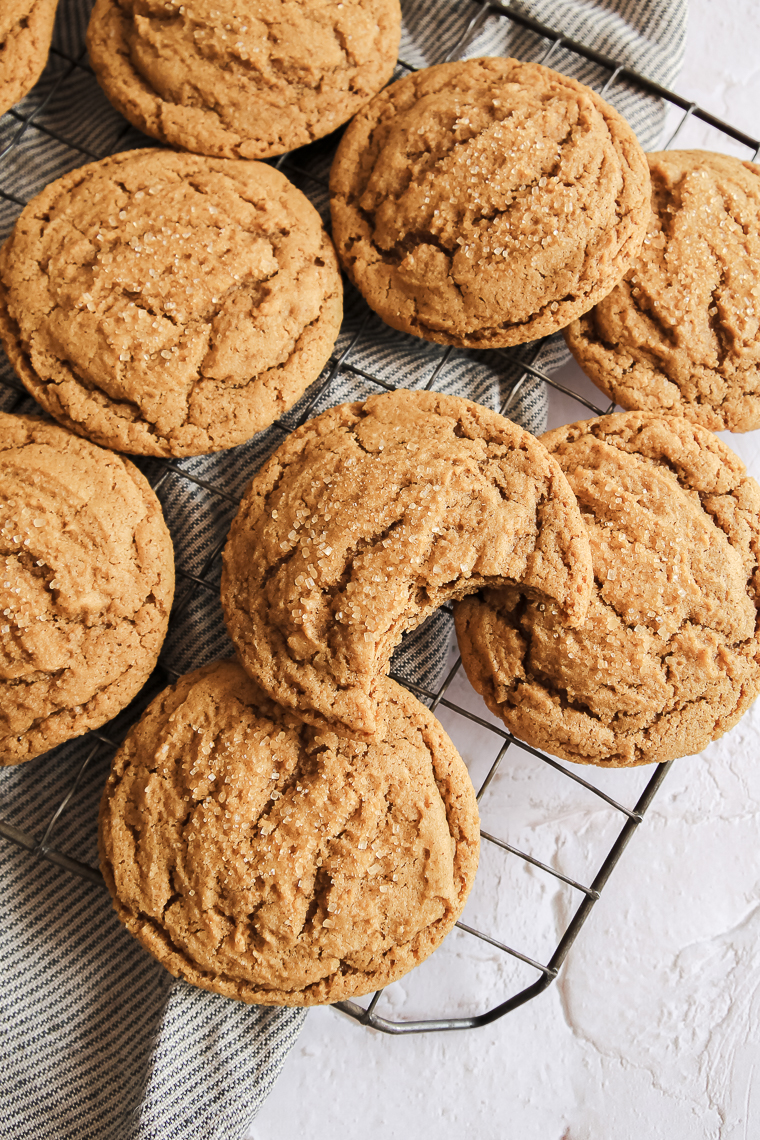 whole wheat molasses cookies on a cooling rack, one with a bite taken out of it to show the soft center.