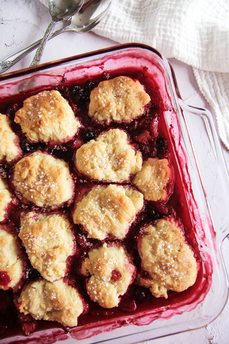 a baking dish full of sourdough old fashioned berry cobbler next to two spoons and a white tea towel