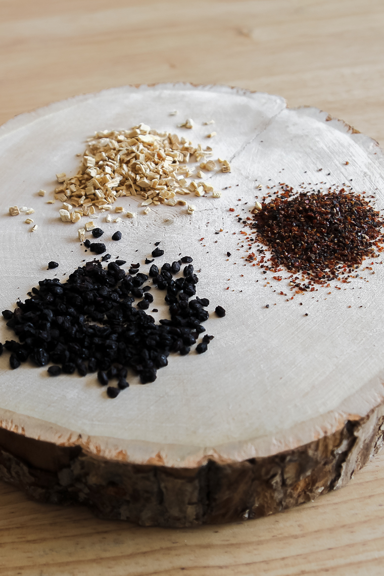 astragalus root, cut and sifted rose hips, and dried elderberries on a wooden trivet