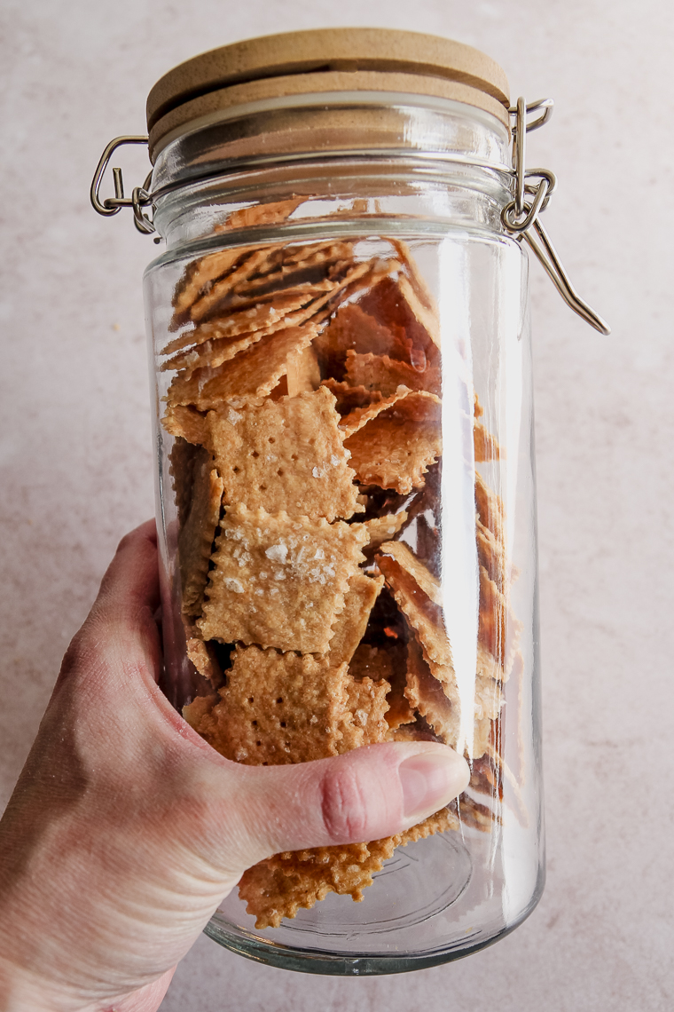 a hand holding a jar of homemade baked einkorn crackers